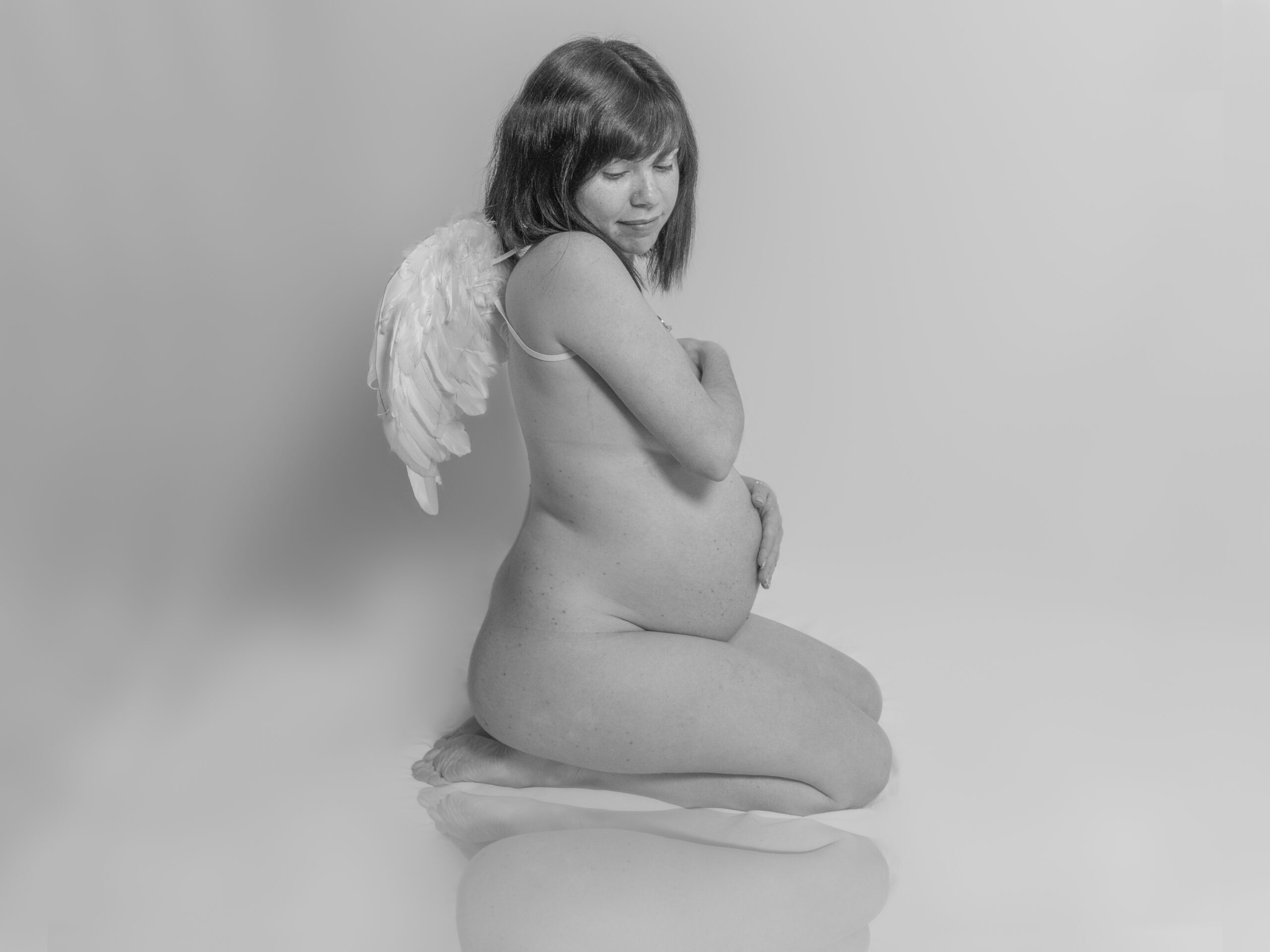 pregnant woman posing with baby belly in photography studio wearing angel wings - maternity photography by Jamie Simmons