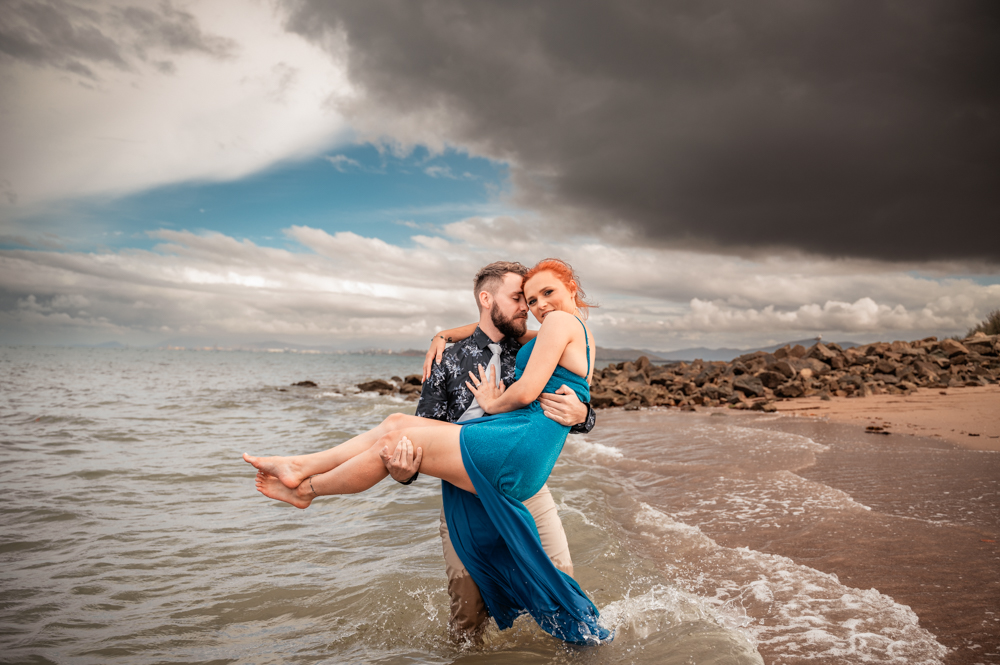 man carrying his fiancé through the water at a townsville beach - engagement photography by Jamie Simmons