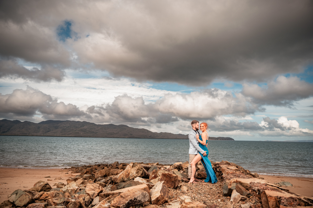 man and woman embracing on a rock wall at a townsville beach - engagement photography by Jamie Simmons