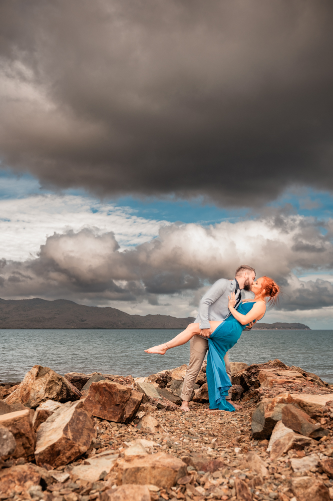 man and woman standing on a rock wall at a townsville beach sharing a kiss - engagement photography by Jamie Simmons