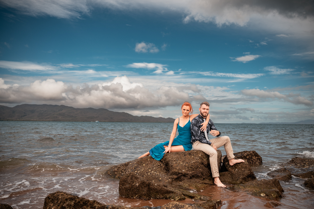man and woman sitting on a rock on a townsville beach as the waves slowly roll in - engagement photography by Jamie Simmons