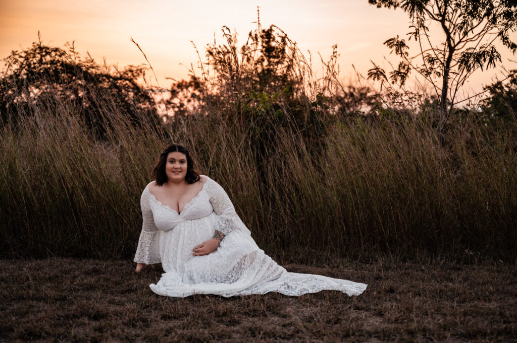 woman in white maternity gown on the grass in a paddock at sunset - maternity photography by Jamie Simmons