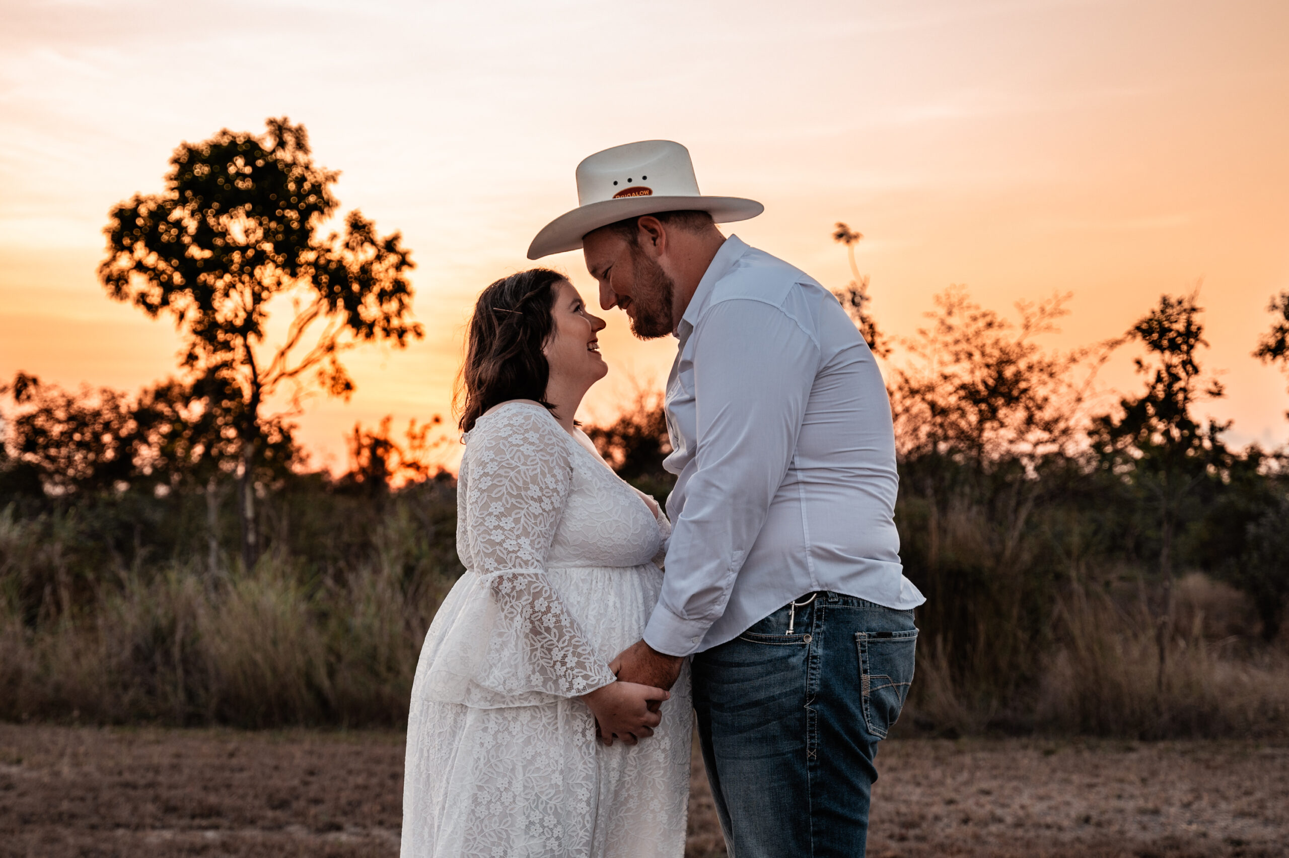 close up shot of pregnant woman in white maternity gown with her partner in the townsville outback embracing baby bump at sunset - maternity photography by Jamie Simmons