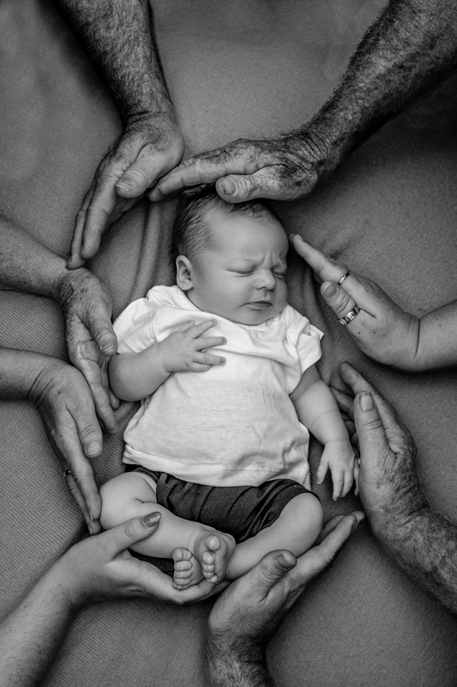 baby boy lying in the middle of a circle mad by the hands of his family- newborn baby photography by Jamie Simmons