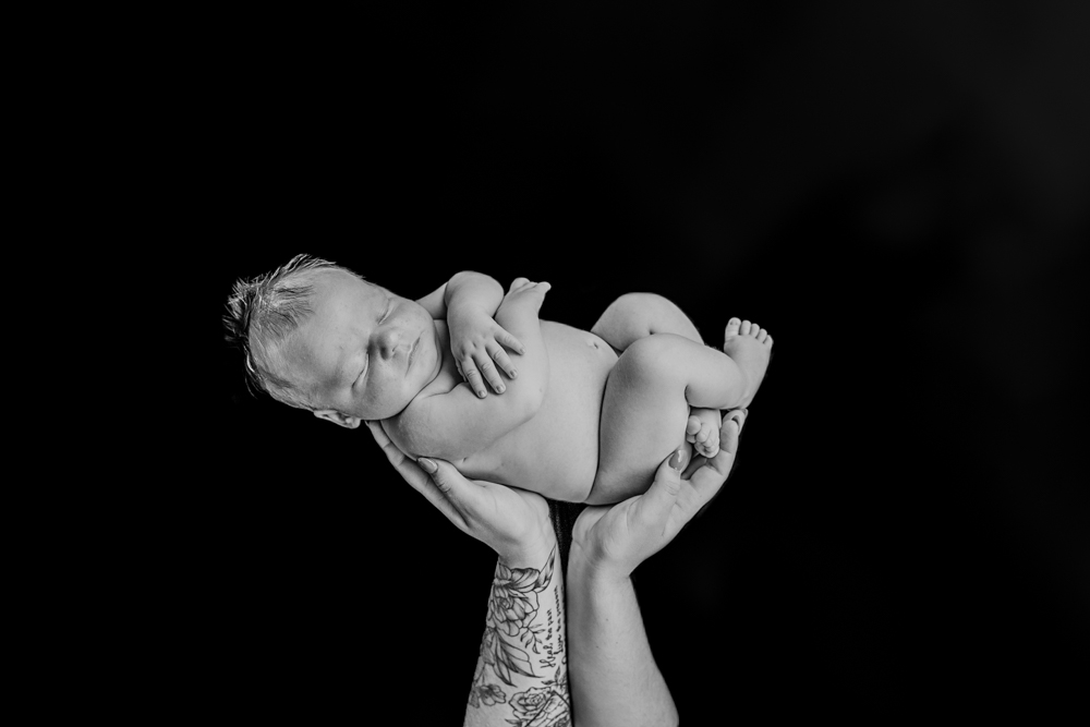 monochrome shot of newborn baby in mums hands against black background - newborn baby photography by Jamie Simmons