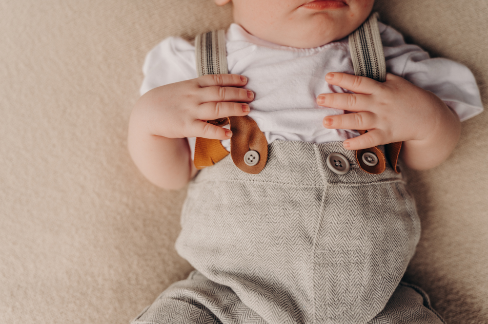 close up shot of baby boy in conductor outfit holding his suspenders - newborn photography by Jamie Simmons