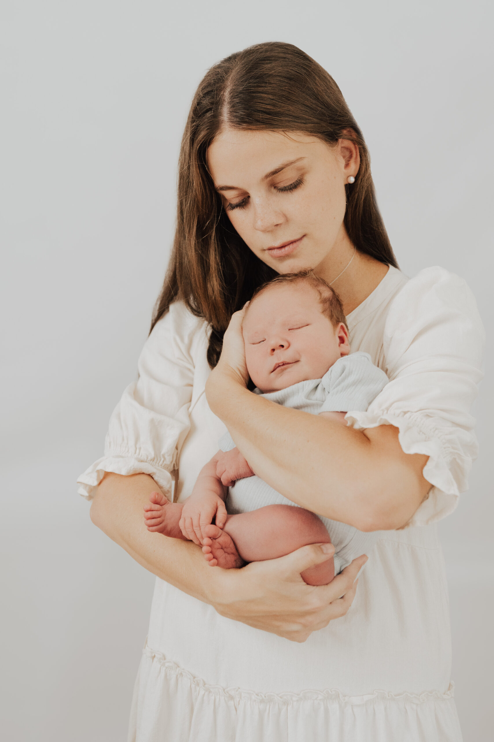 newborn baby being held close by mum in white dress - newborn photography by Jamie Simmons
