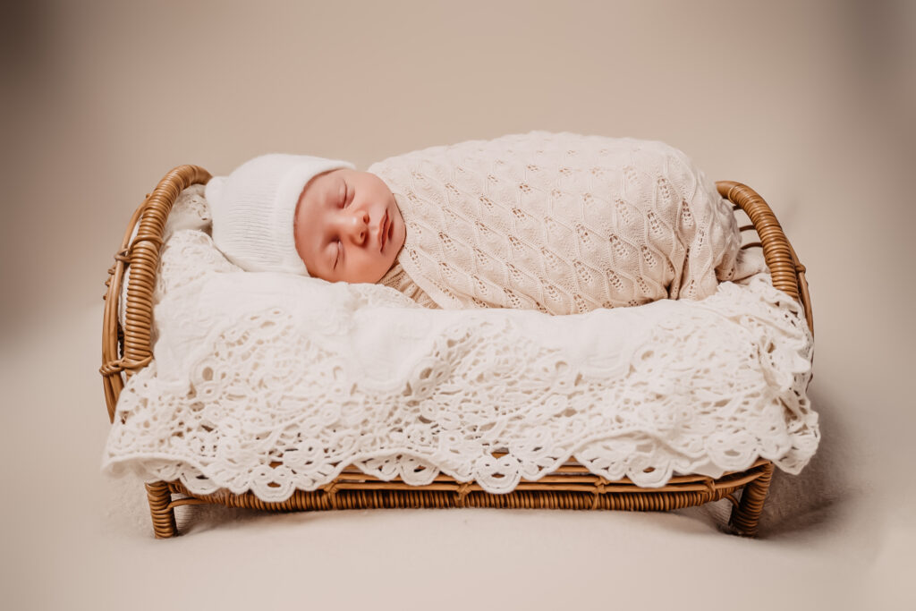 newborn baby wrapped in comfort wrap and posed on doll bed while wearing a sleepy hat - newborn photography by Jamie Simmons