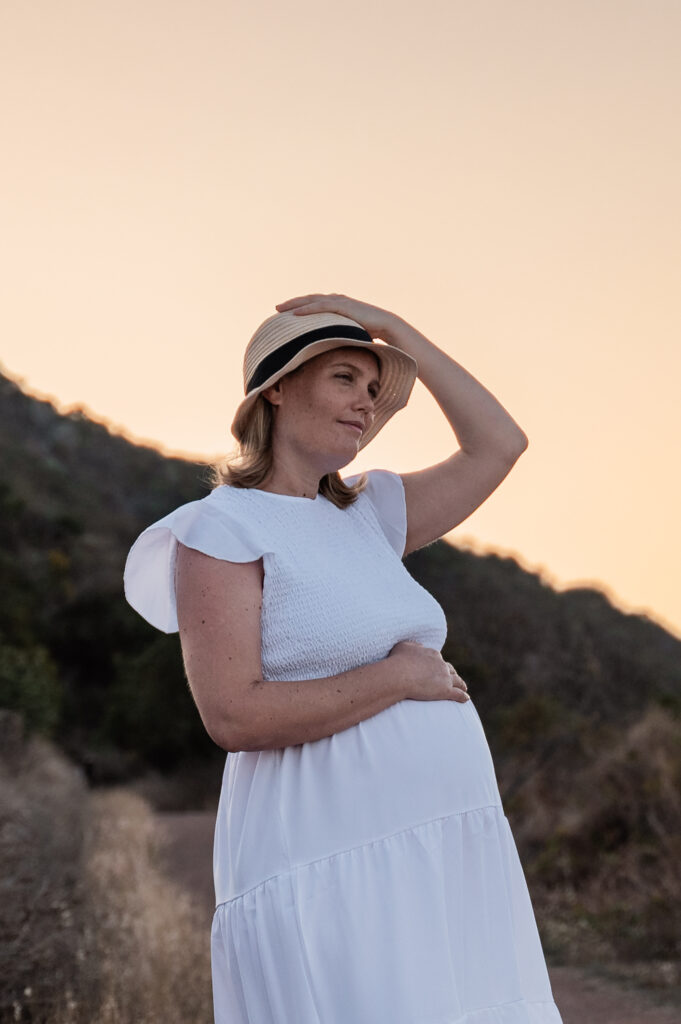 pregnant woman in white maternity gown on the hills in townsville at sunset embracing her baby belly - maternity photography by Jamie Simmons