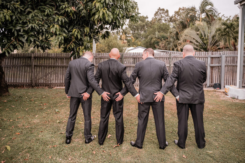 Groomsmen in tailored suits stand proudly in a lush yard, capturing a moment of unity and celebration before the wedding - by Jamie Simmons