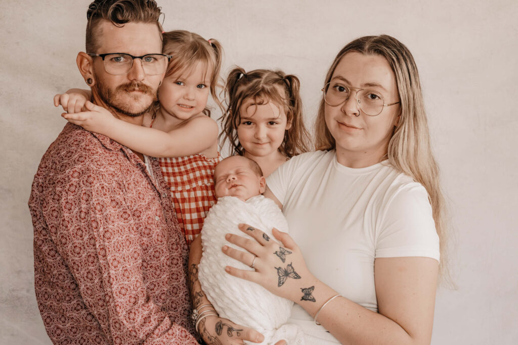 A happy family stands together with their newborn, beautifully captured by Townsville's Simmons Memorable Moments.