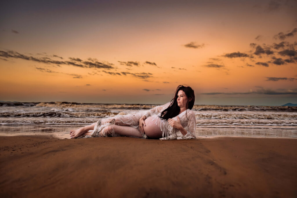 Sunset beach view with a pregnant woman resting, taken by Simmons Memorable Moments, specializing in Townsville motherhood.