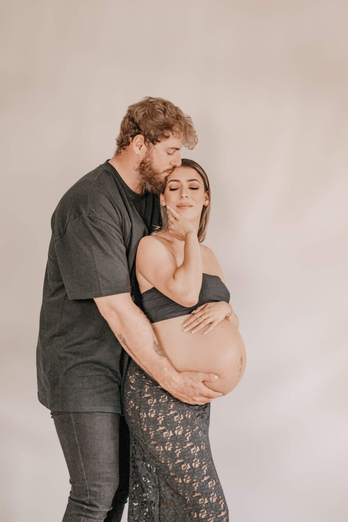 A pregnant couple poses together against a white background, captured by Simmons Memorable Moments, Townsville Motherhood photographer