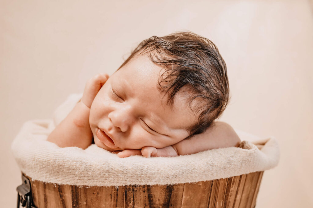 Newborn baby sleeping in a rustic wooden bucket prop, styled on a soft cream backdrop by Simmons Memorable Moments, Townsville